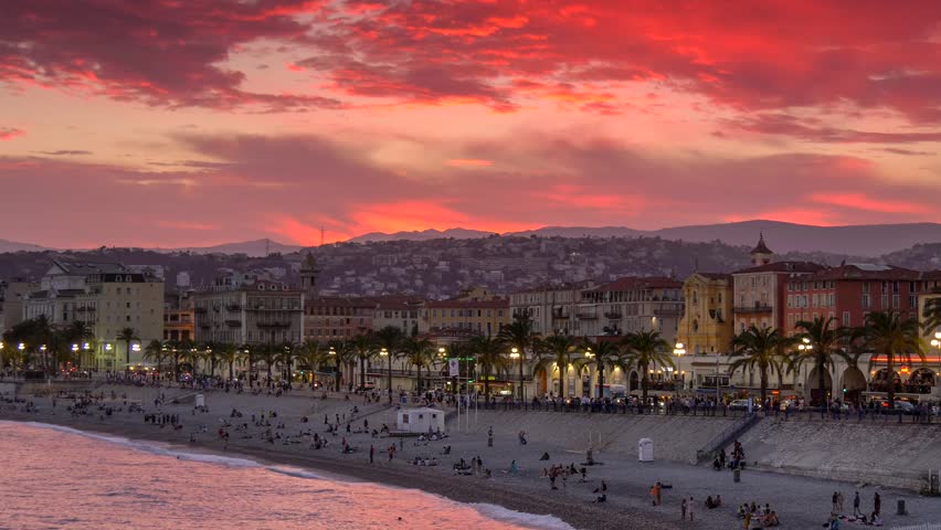 Beautiful sunset view of Nice, France. Beach and embankment with red sky background.