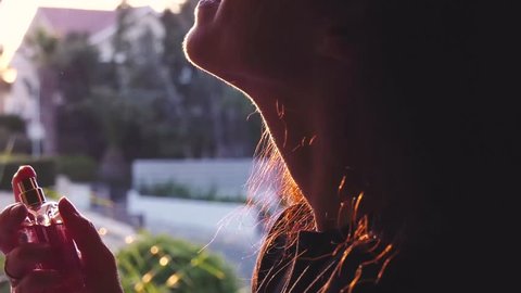 girl spraying perfume on neck against evening light 