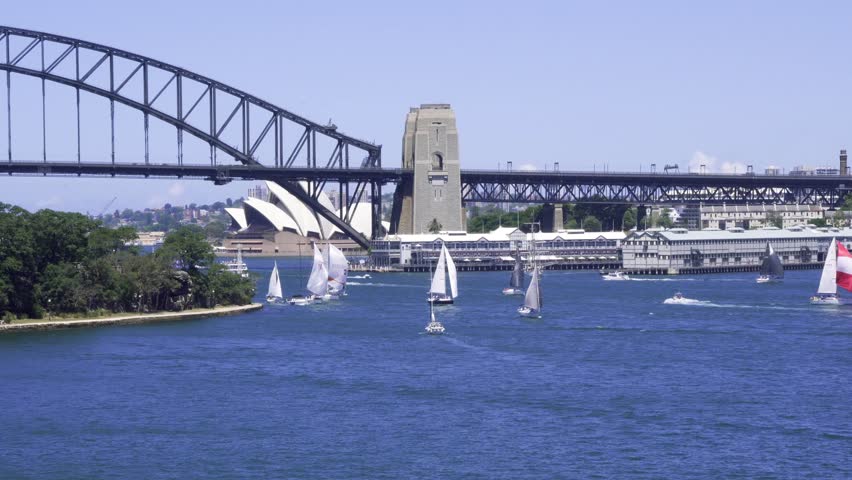 Sydney Opera House concert hall and famous harbour bridge behind sailing boats yachts racing across the beautiful harbor harbour on a sunny day.