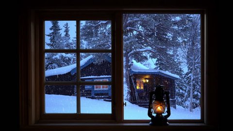 A woman carrying a lantern walking by a mountain cabin in wintry conditions seen through a window.