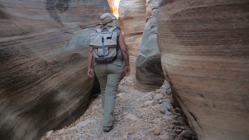 Active woman hiking through the dried up narrow stone gorge of river with smooth and wavy rocks of a colorful canyon zion national park, looks around and expresses emotions slow motion, 4K, 3840X2160