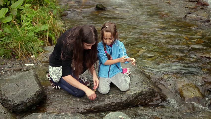 Mother and daughter collecting, picking up pebbles from mountain river bank stones and gems
