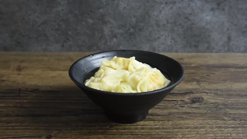 Video of preparing Chinese type of noodles and Shrimp Wonton with soup are sprinkled onion to add flavor and smell delicious on the wooden table.