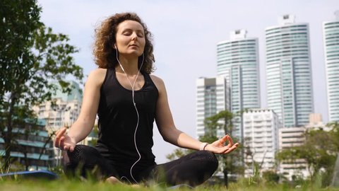 Young Woman In Earphones Doing Meditation In City Park.