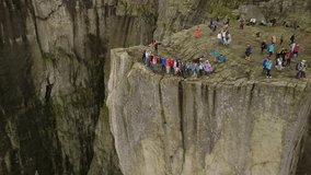 Aerial view from drone on breathtaking cliff called Preikestolen. Group of young people is standing on the edge of cliff and making the waves with hands. 4k footage, upper view. Norway.
