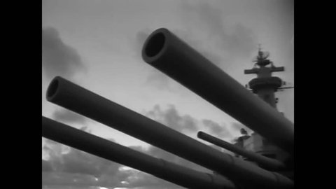 CIRCA 1950 - The UN flag is hoisted on the USS Missouri, while sailors load projectiles into the breach.