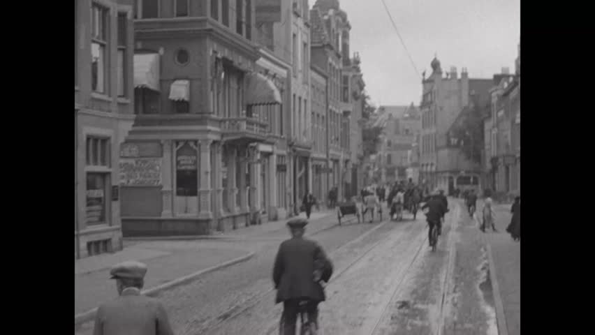 CIRCA 1910s\xD1Pedestrians and cyclists travel down a street in shopping district in Groningen, Netherlands.