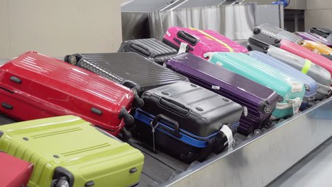 Suitcases on moving luggage conveyor belt at arrival area of passenger terminal. Colorful bags on baggage carousel.