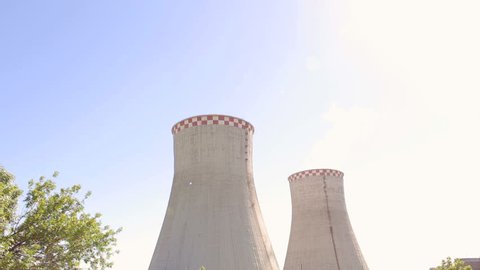 Huge cooling towers of brown coal power plant at background of industrial landscape. Nuclear power plant on the sky background in sunlight. Two cooling towers in a field in the bright sun. Industry.