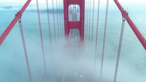 Bird view of the fog going through the famous Golden Gate Bridge. Aerial of the towers of the red bridge with vehicle traffic and yacht going by in the San Francisco Bay on a misty day. California, 4K
