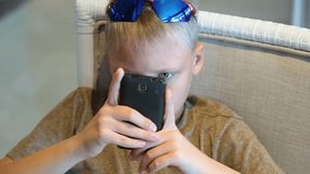Funny cute kid playing games at smartphone. Child of 10 years old holds phone too close to his face. Real time full hd video footage.