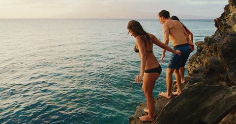 Friends cliff jumping into the ocean at sunset Arkivvideo