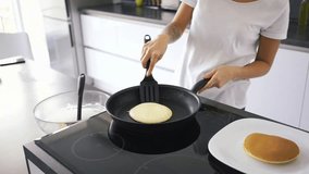 Cropped view of a smiling asian woman standing by the stove on kitchen and cooking pancakes