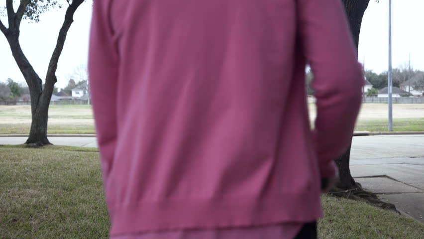 A Caucasian senior citizen woman with a cane walking away slowly and carefully on a neighborhood sidewalk.
