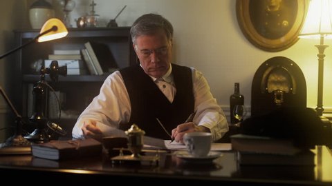 Period piece 1930s home office scene lit by lamplight of tired mature businessman at the end of the workday who puts down a fountain pen and pours himself a drink. Dolly movement.