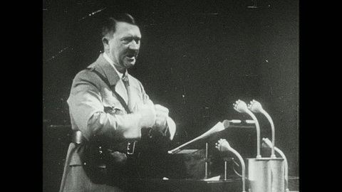 1940s: Adolf Hitler gives speech, gesticulates with closed fists. Fly's head. Tojo stands and gets flashed from cameras. Boll weevil. Bennito gives a speech and stands with his hands on the belt.