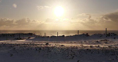 Snow drifting by rocky farmland fence, Icelandic coast winter.
