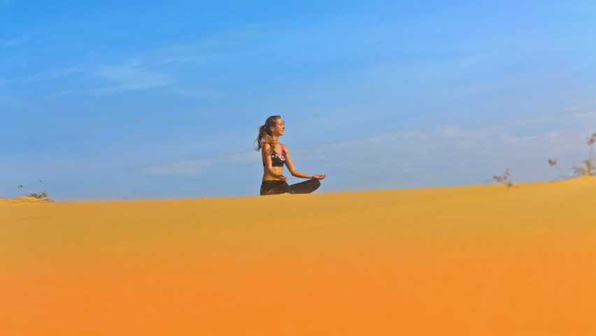 wonderful view from below young beautiful girl sits in meditative pose on gold sand against blue sky