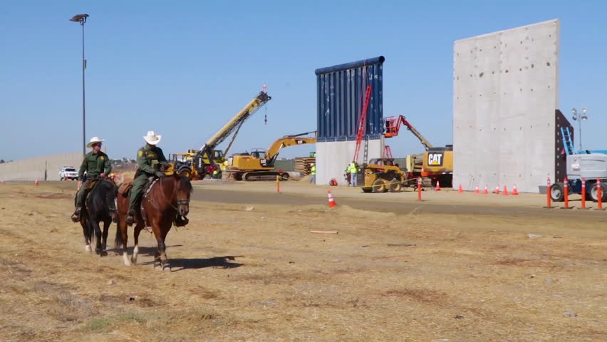 CIRCA 2010s - Horsemen from the US Border Patrol ride beside Trump border wall prototypes along the U.S. Mexico border.
