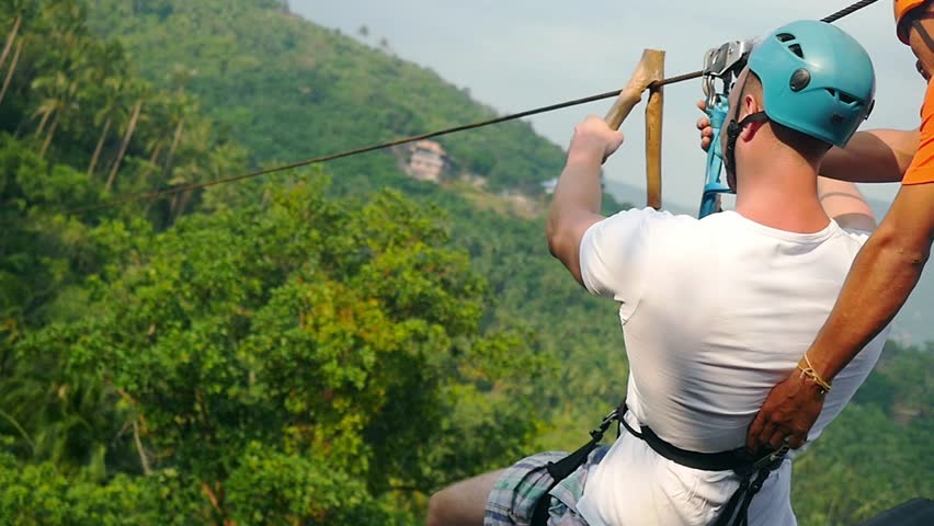 Tourist man in helmet slides a rope descent above beautiful tropic forest in jungle. slow motion. 1920x1080