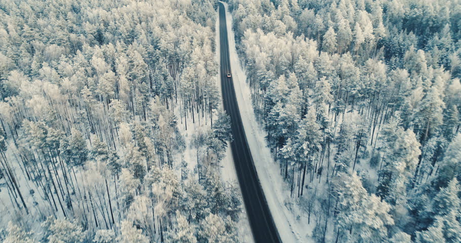 Aerial view of a car driving on a snowy forest road. 4K.