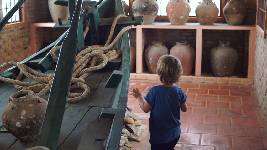 Little boy visits exposition in national museum on Phu Quoc island Vietnam, he looks at an ancient boat filled with ceramic jugs
