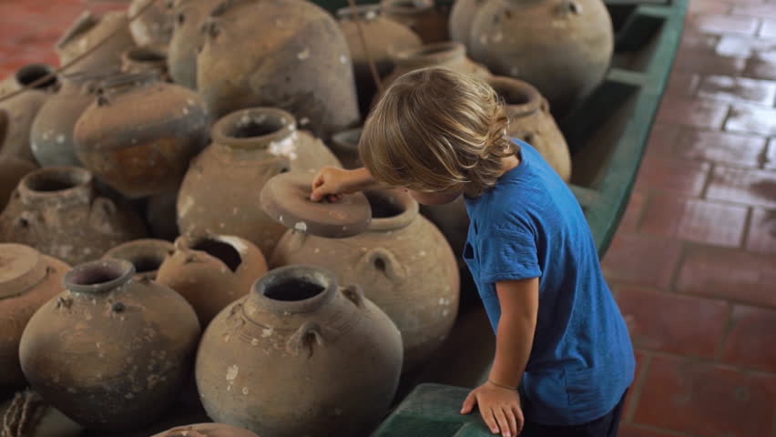 Little boy visits exposition in national museum on Phu Quoc island Vietnam, he looks at an ancient boat filled with ceramic jugs