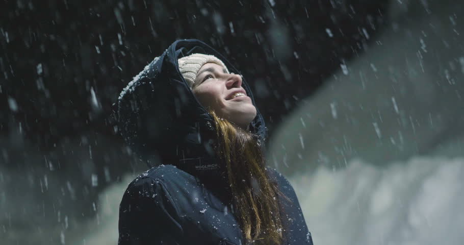 As the snow falls from the sky, a beautiful woman at night stops in a light and starts playing, breathing clean air and dancing in the middle of nature.