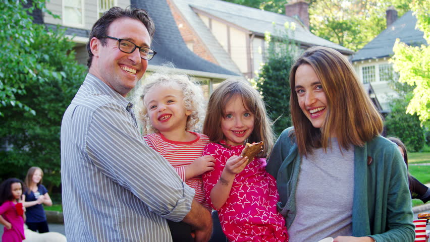 Parents holding young kids smile to camera at a block party