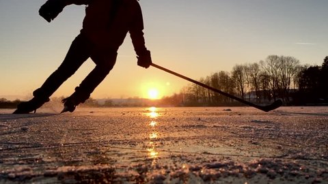 Panoramic slow-motion action footage of a male 
hockey player skating on a frozen lake in beautiful golden evening light at sunset in winter