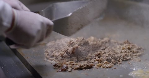 Cooking and chopping an authentic Philly Cheesesteak on a restaurant griddle, in slow motion
