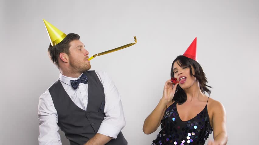 celebration, fun and holidays concept - happy couple with party blowers and caps