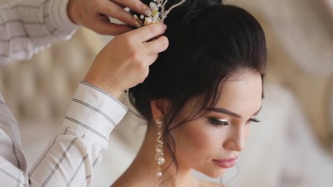 Stylist finishes a hairstyle the pretty young bride at wedding day in slow motion.