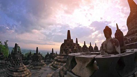 Scenic panoramic view of Borobudur temple at sunrise with beautiful sky and Buddha stone sculpture in meditation pose sitting in buddhist stupa. Traveling to Java Indonesia