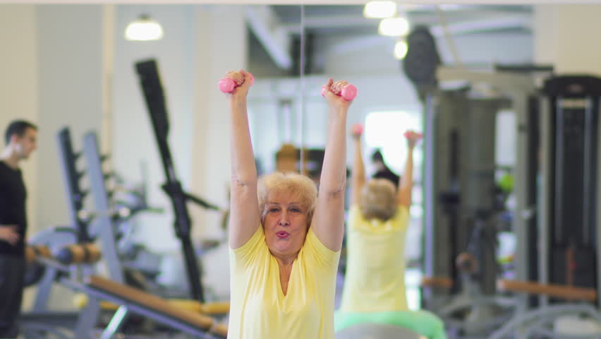 Granny makes exercise with barbell in the gym