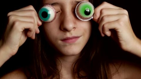 close-up. a cheerful teenage girl brings a big round candy to her eyes, similar to eyes. 4k.