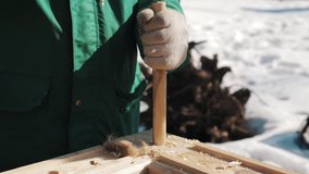 Close up hand in worker gloves hammering wood kernel to hole in wooden block outside in winter, snow on background