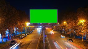 A billboard with green chroma key on a background of a city night landscape of fast moving cars with long exposure. Time Lapse video. The camera is approaching