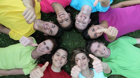 Happy joyful group of frined staying together outdoor. Smiling teenagers forming a circle of head lying on back. Portrait of group of people exults lying on grass at park and looking at camera.