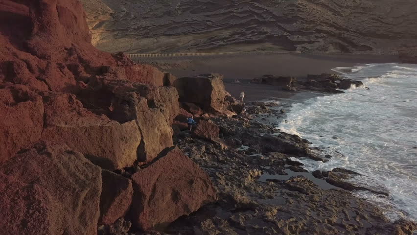 Aerial footage of girls climbing on the rocks  on the beach on the ocean