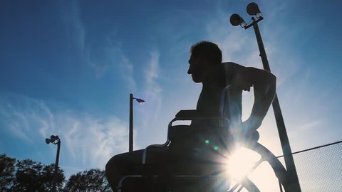 Silhouette of disabled athlete in wheelchair playing tennis outdoors 