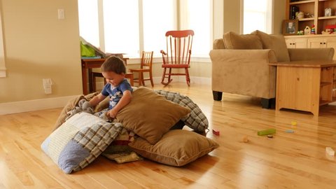 A toddler builds a blanket and pillow fort on the floor of his home to play