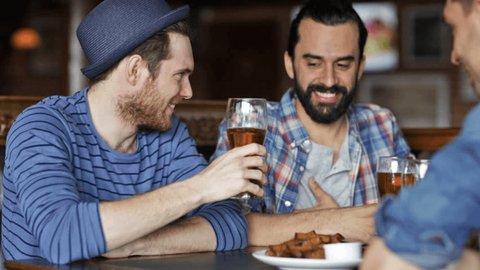 people, leisure, friendship and celebration concept - happy male friends drinking beer, eating bread snack and clinking glasses at bar or pub