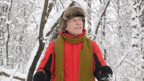 Elderly Caucasian smiling man with Hiking Sticks walks through a snowy forest. Portrait video shooting. Thick dense thicket of trees and roots in in the snow-covered forest. Hike and travel concept 60