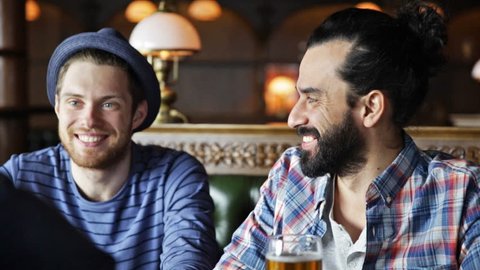 people, toast, leisure, friendship and celebration concept - happy male friends drinking beer and clinking glasses at bar or pub