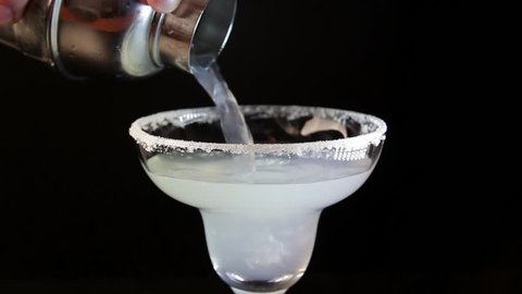 Process of serving margarita cocktail. Bartender pouring alcohol drink into a glass close-up.