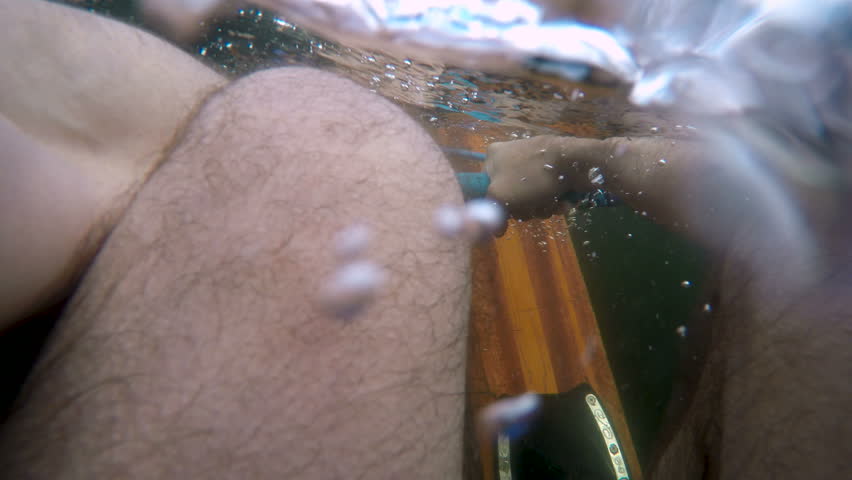 POV of a man trying to get up on vintage wooden water skis and crashing back underwater in a lake