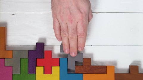 Top view on man's hand playing with colorful wooden blocks on the white wooden table background. The concept of logical thinking.