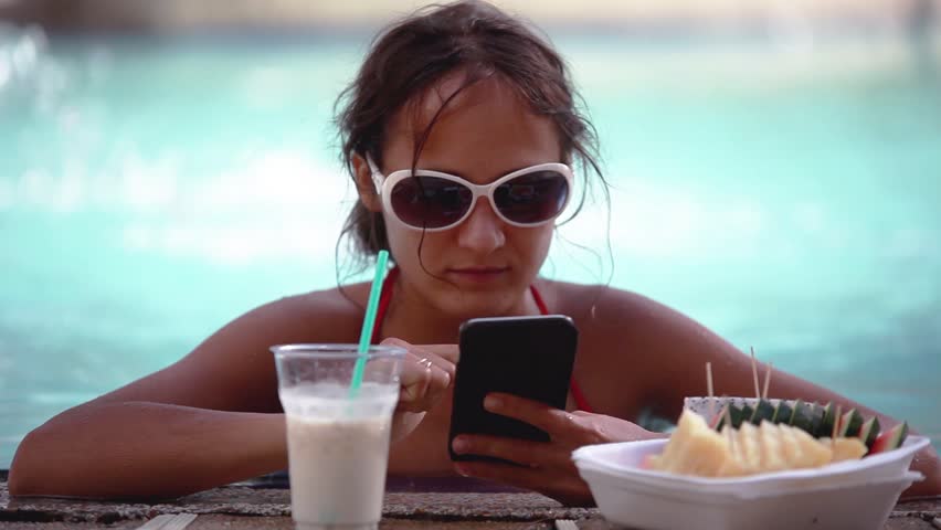 Young pretty woman in sunglasses has chatting with mobile Phone drinks cocktail in swimming pool. HD, 1920x1080.