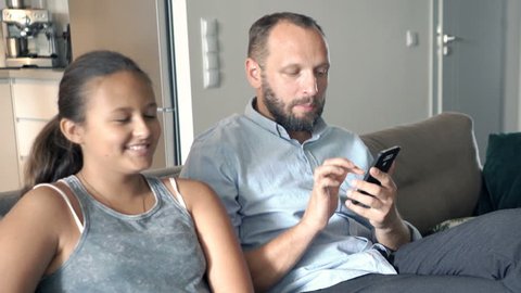 Family talking and using smartphone sitting on sofa at home

